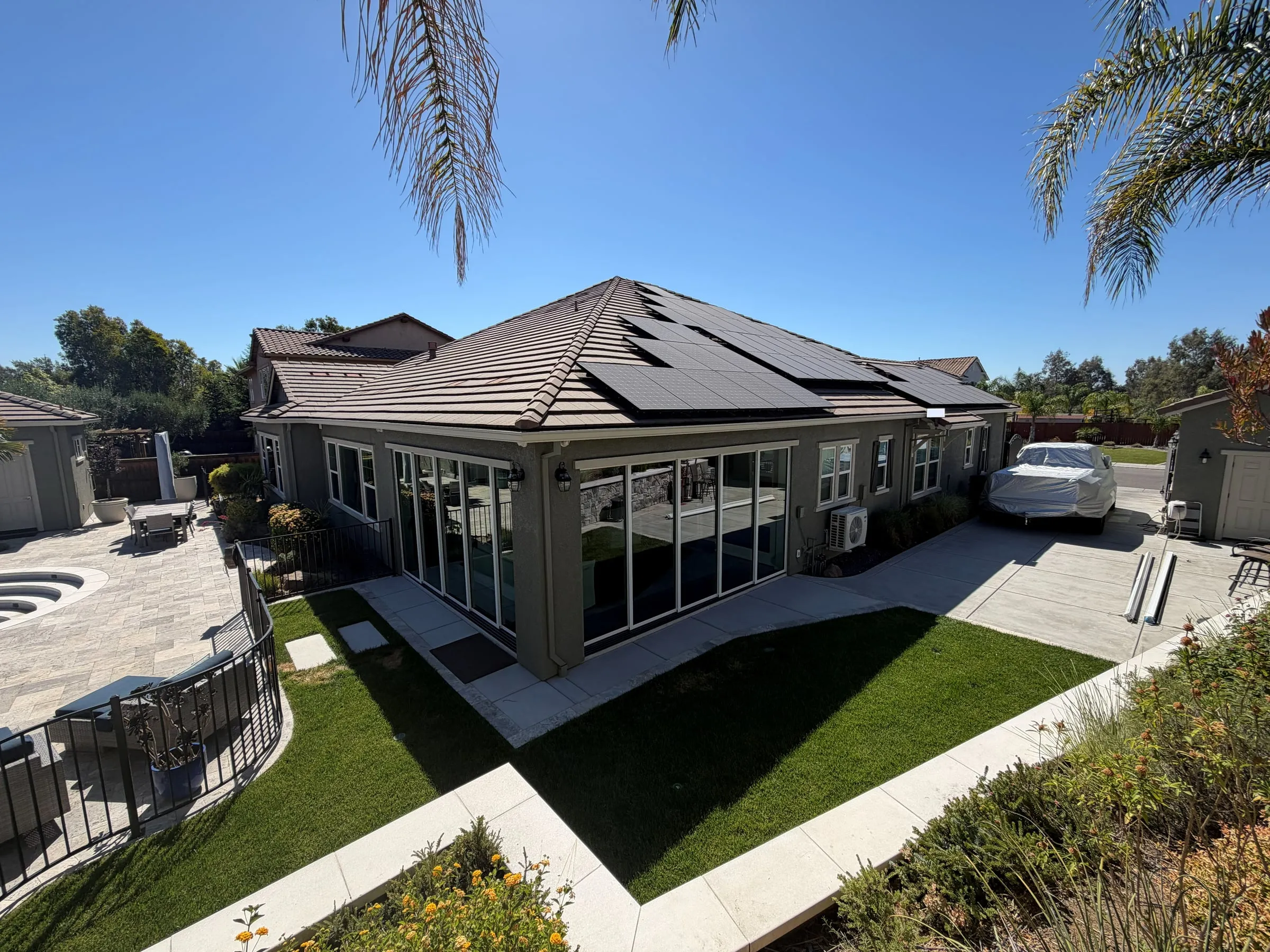 Backyard view of a stucco addition with glass walls beside the lawn, patio and pool area