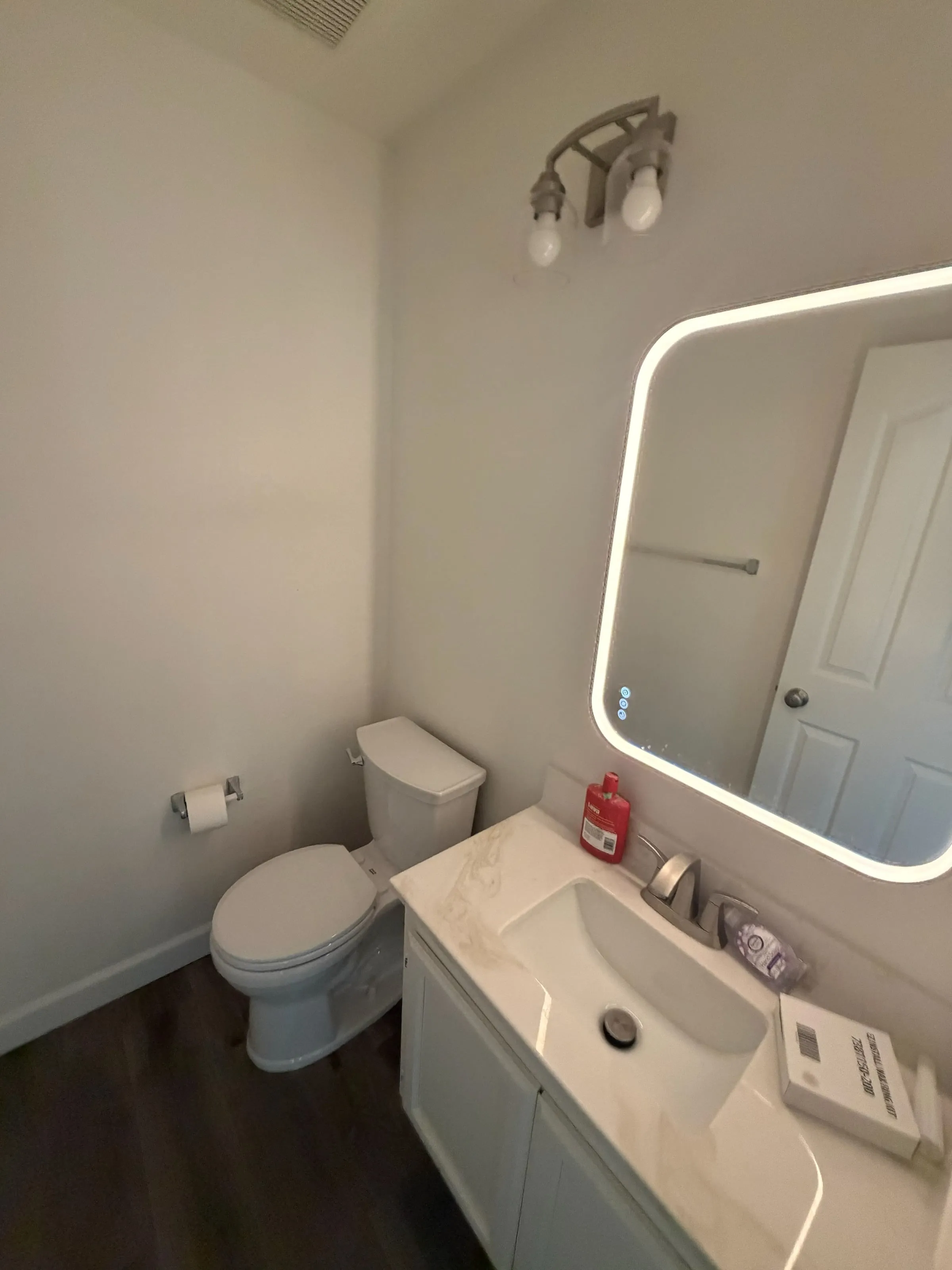 Remodeled bathroom with a lighted mirror, white quartz vanity and plank flooring