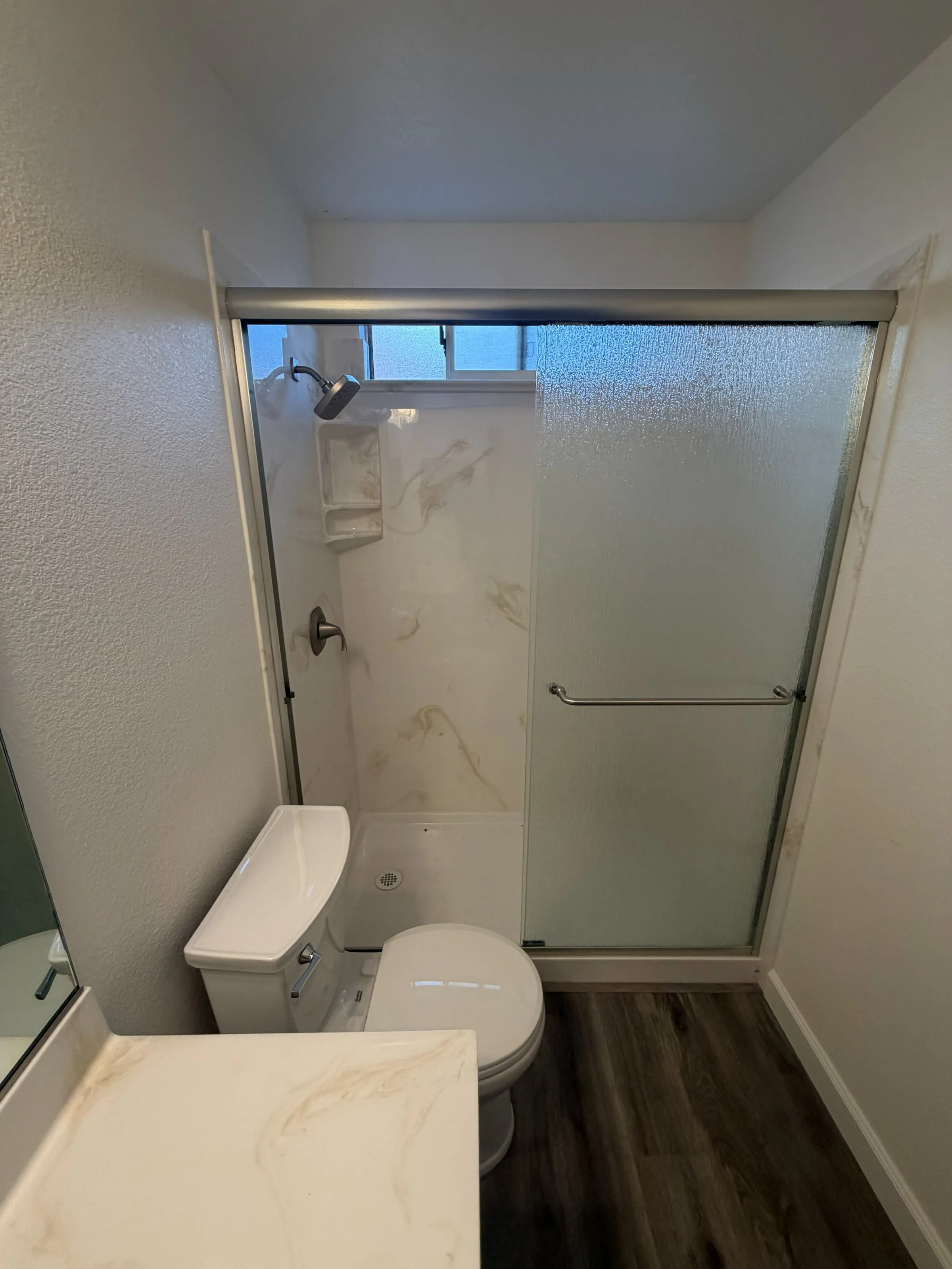 Shower with marble-look wall panels and sliding glass doors in a remodeled bathroom
