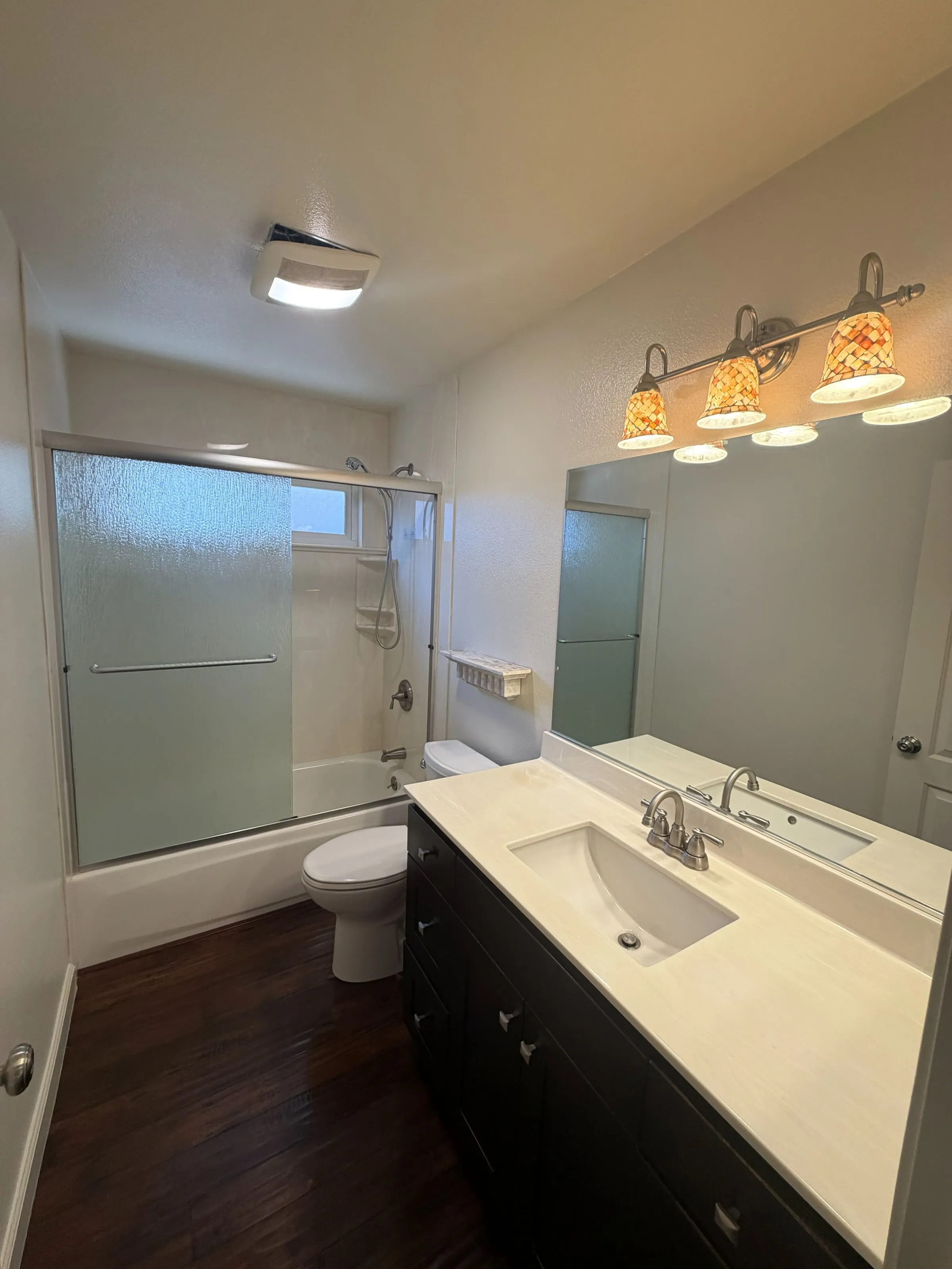 Bathroom with a tub-shower, dark vanity, quartz top and wood floor