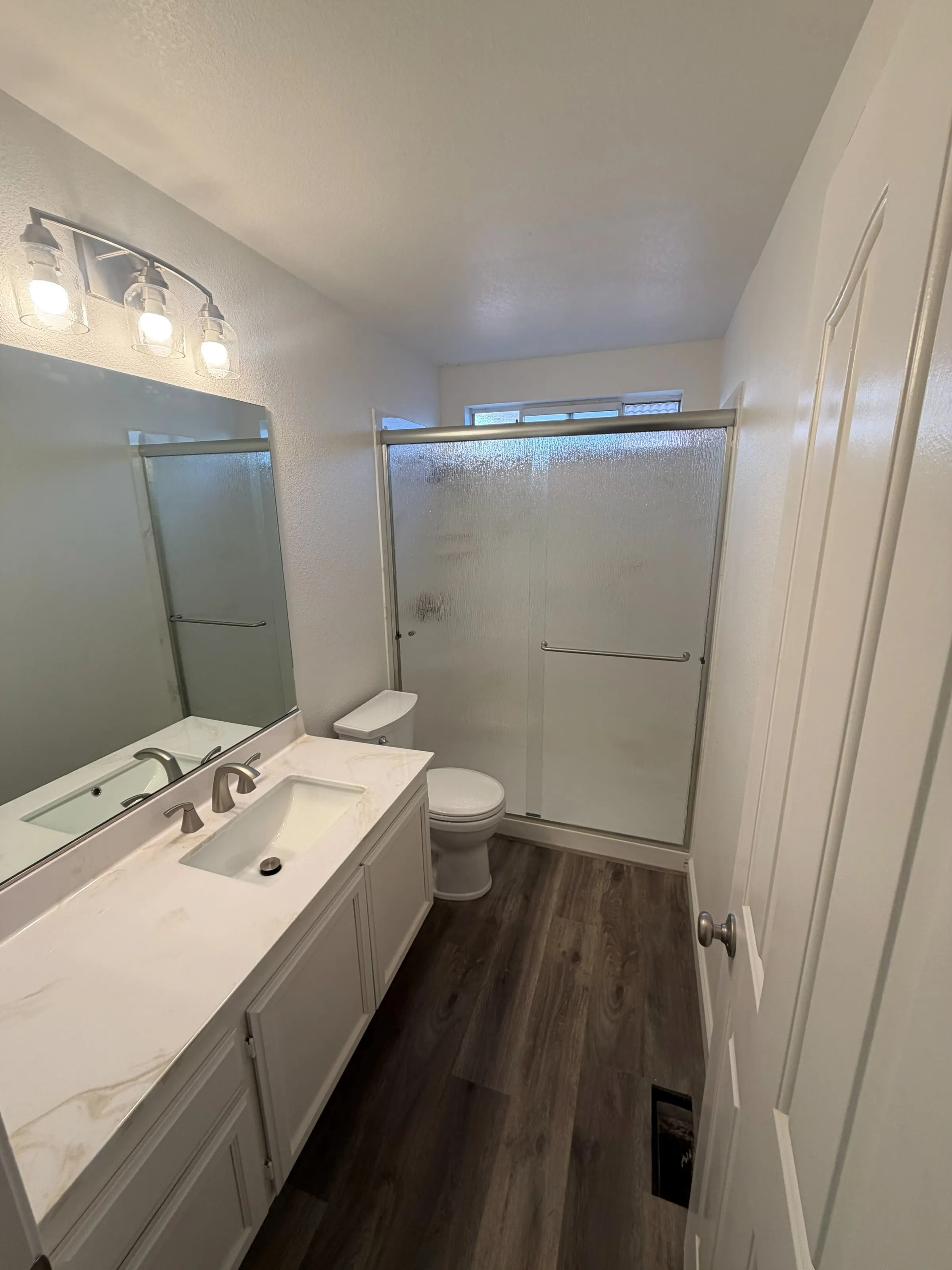 Updated bathroom with a quartz vanity, wide mirror and sliding glass shower doors