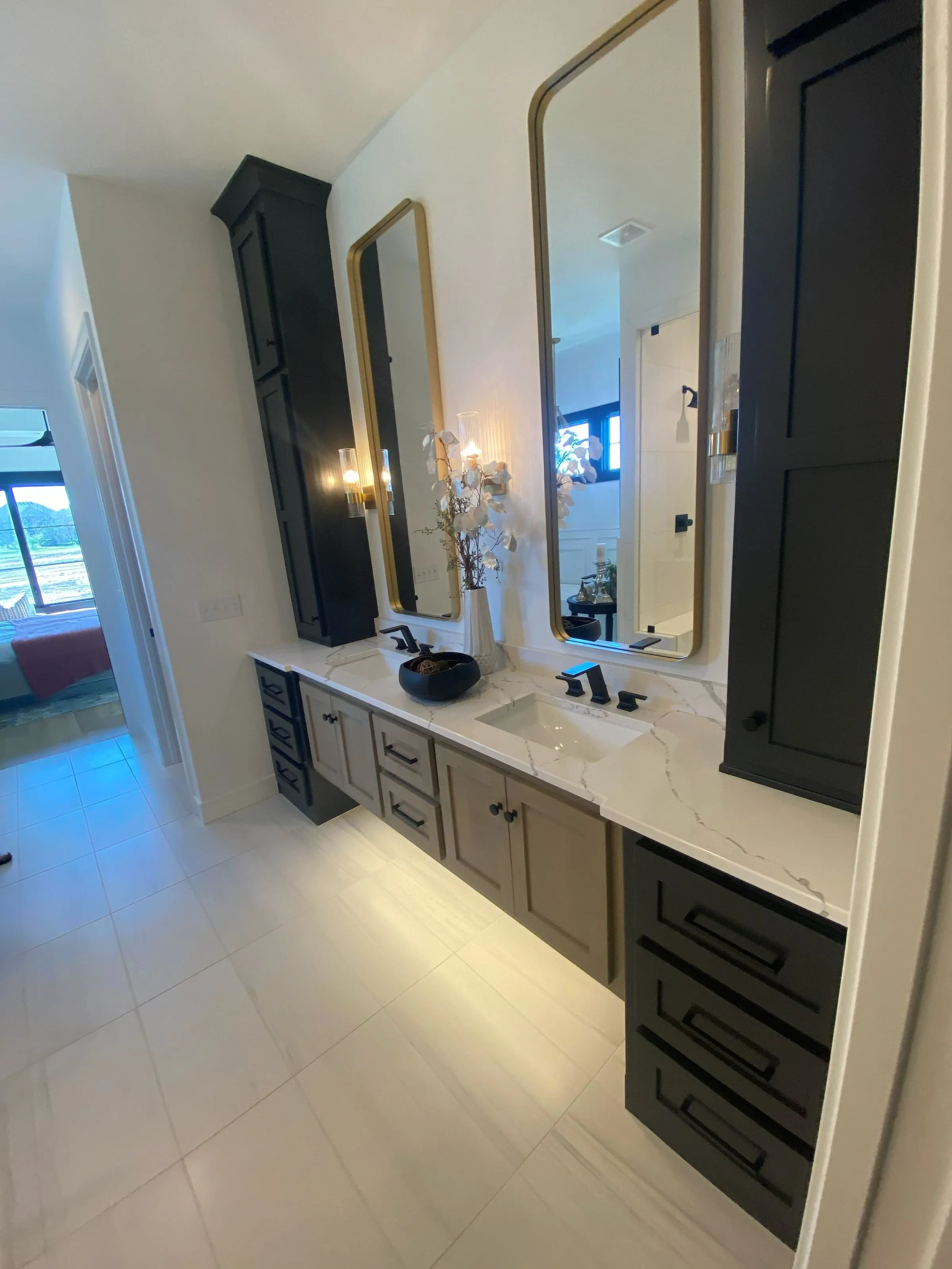 Bathroom vanity with tall black linen cabinets and brass-framed mirrors
