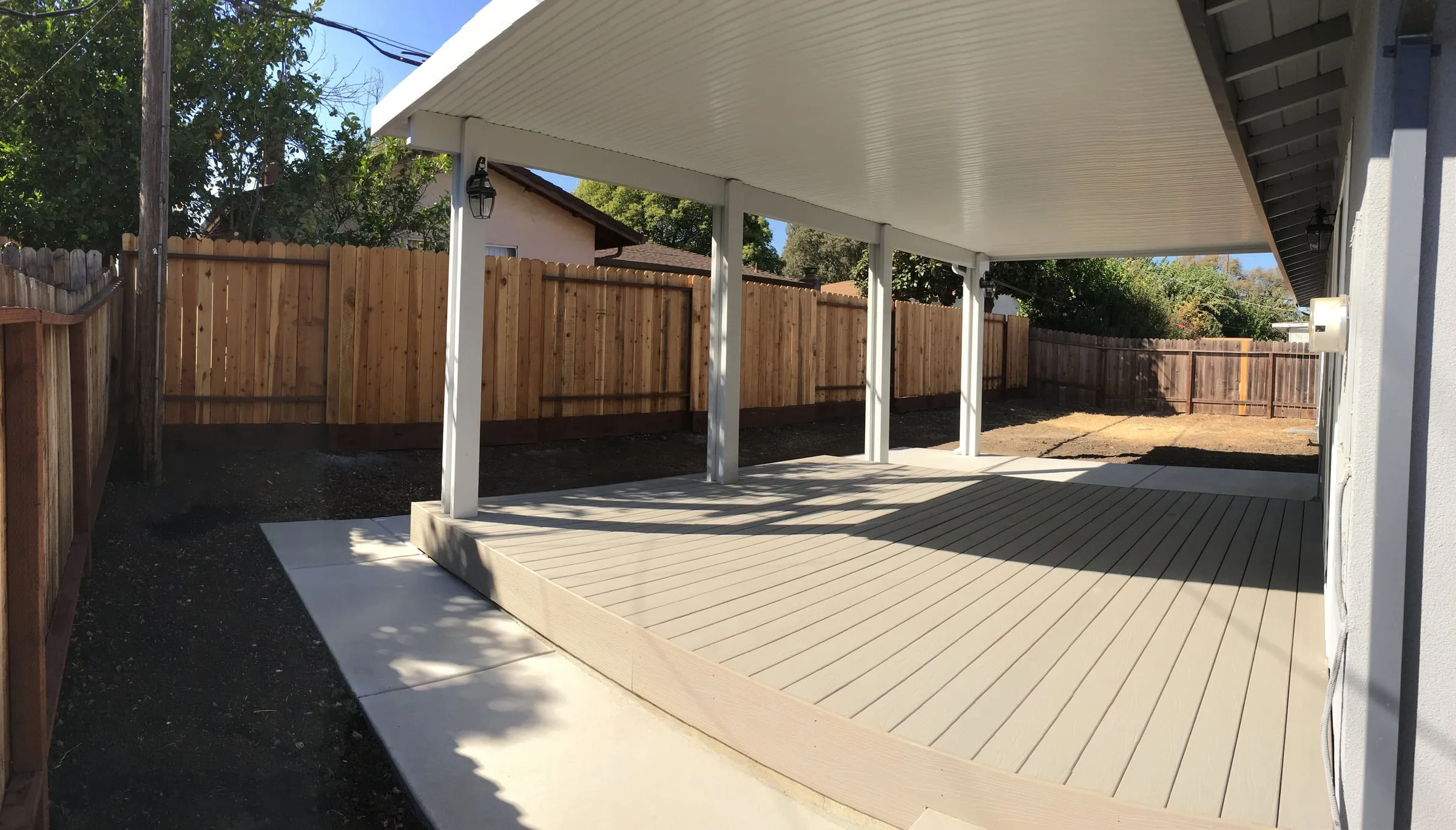 New composite deck under a long white patio cover in a fenced backyard