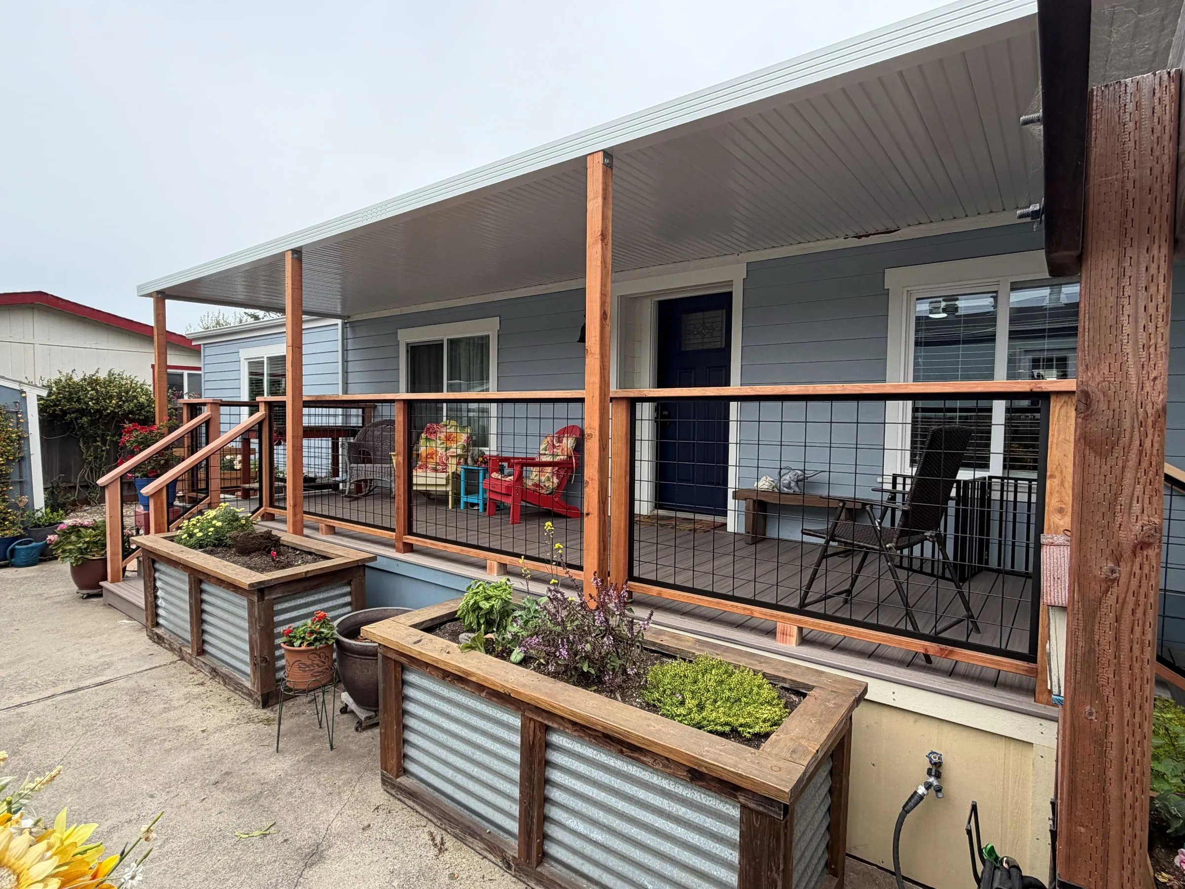 Mobile home porch under a custom patio cover with redwood posts, wire-panel railings and corrugated planter boxes