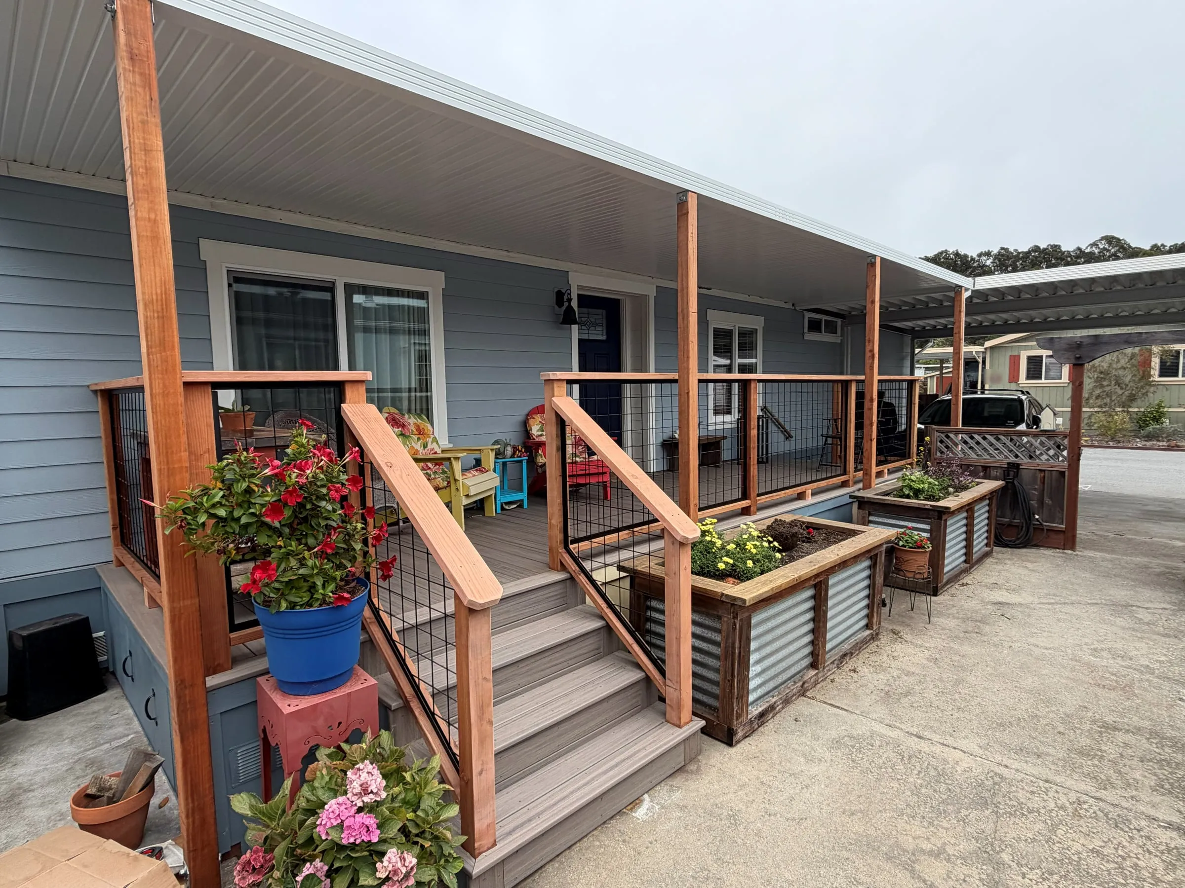 Custom patio cover on redwood posts over composite steps and wire-panel railings at a mobile home