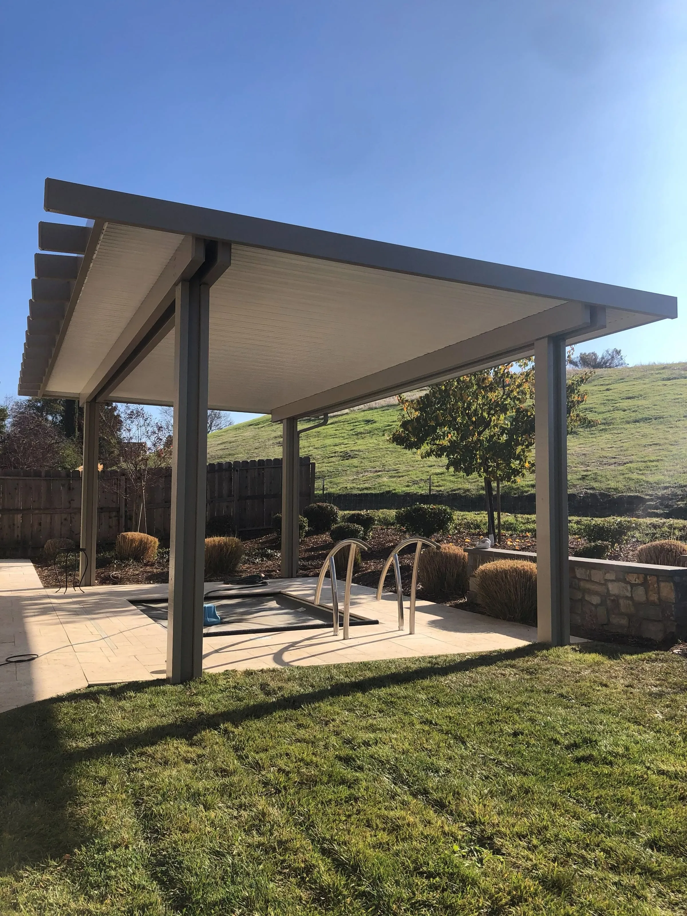 Freestanding patio cover on a concrete pad facing a green hillside