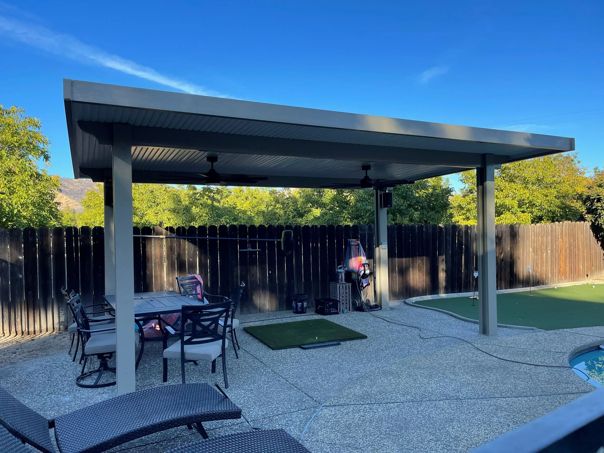 Freestanding patio cover with ceiling fans beside a pool