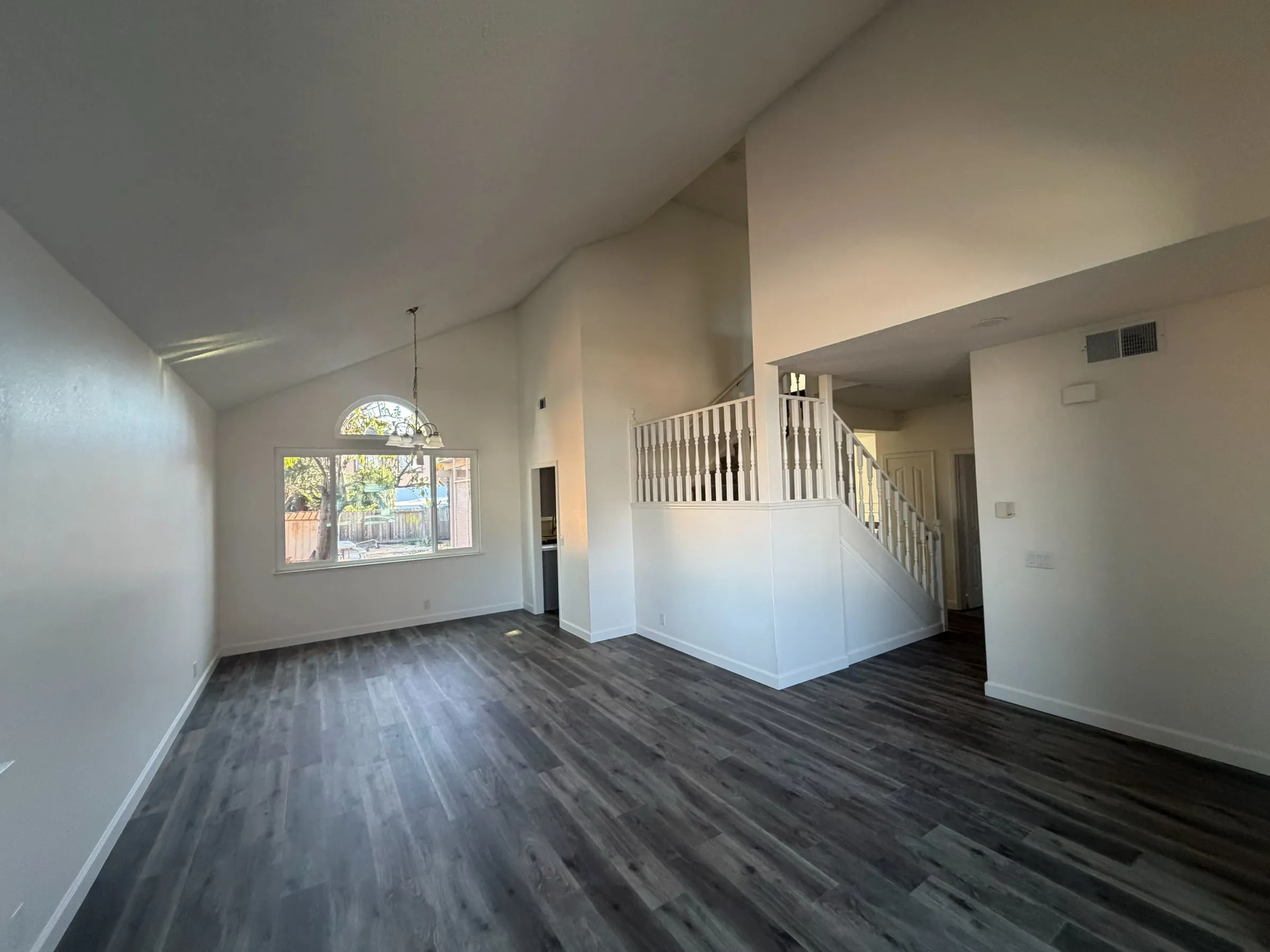 Freshly painted open living area with a vaulted ceiling, arched window and new plank flooring
