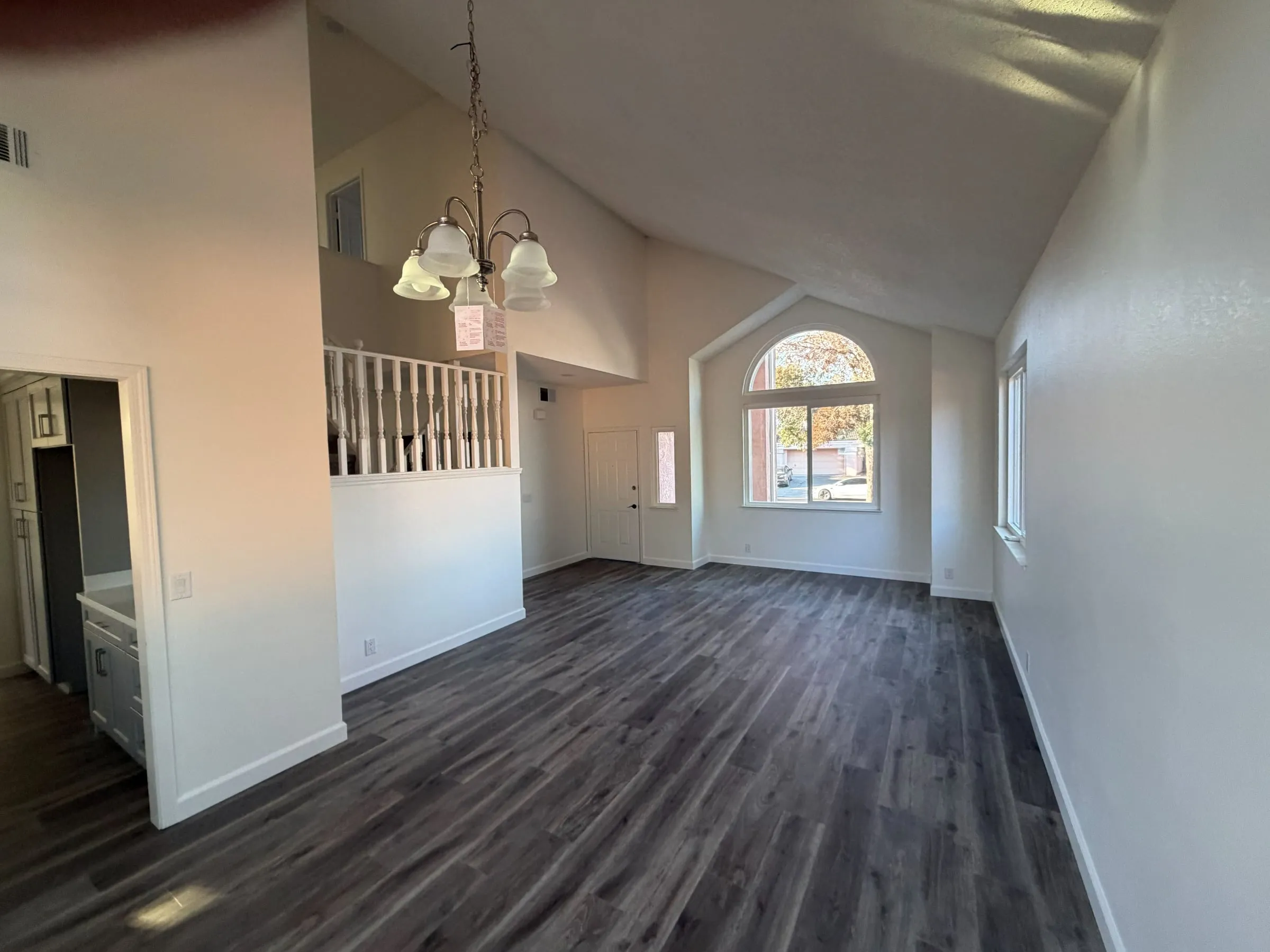 Living room repainted white with a vaulted ceiling, chandelier and new plank flooring