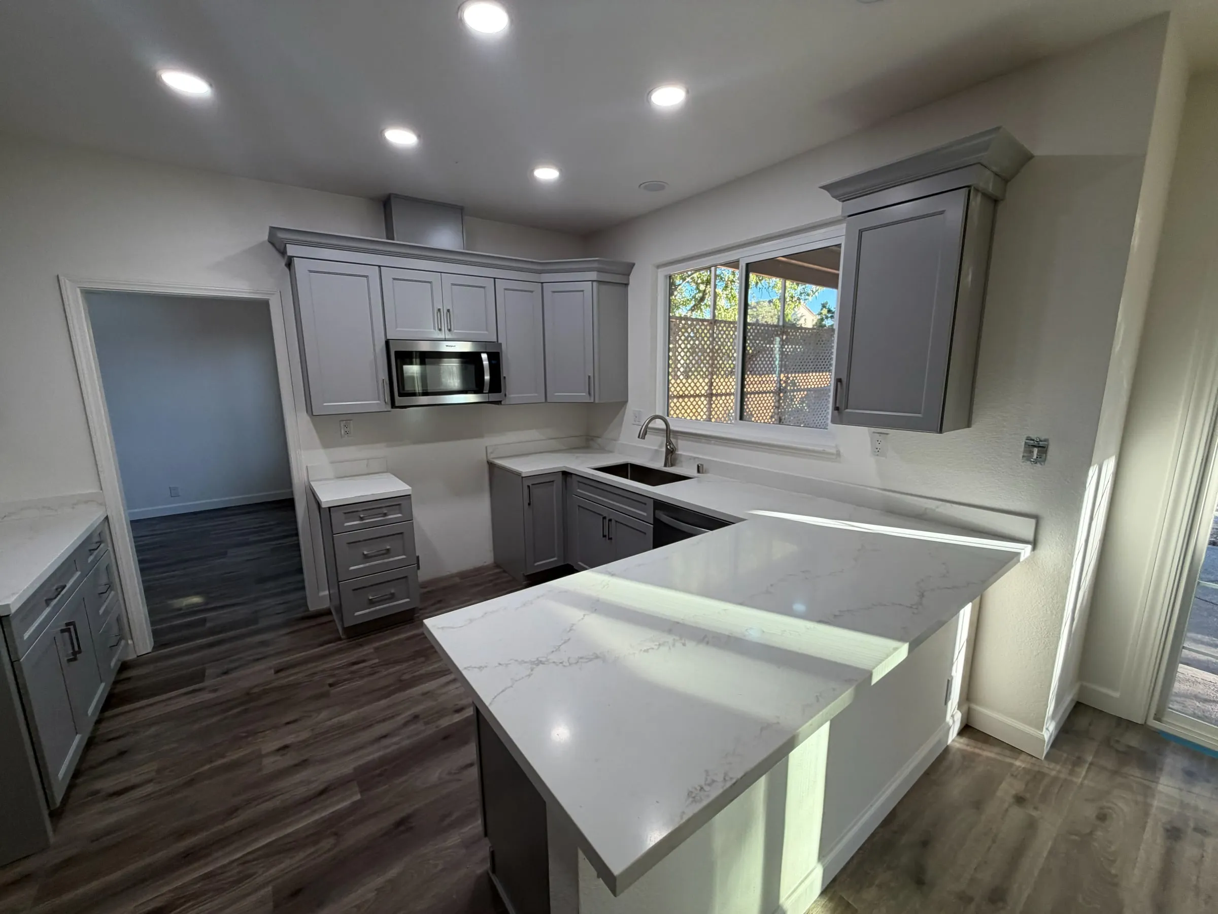 Remodeled kitchen with gray shaker cabinets, a white quartz peninsula, recessed lights and plank flooring