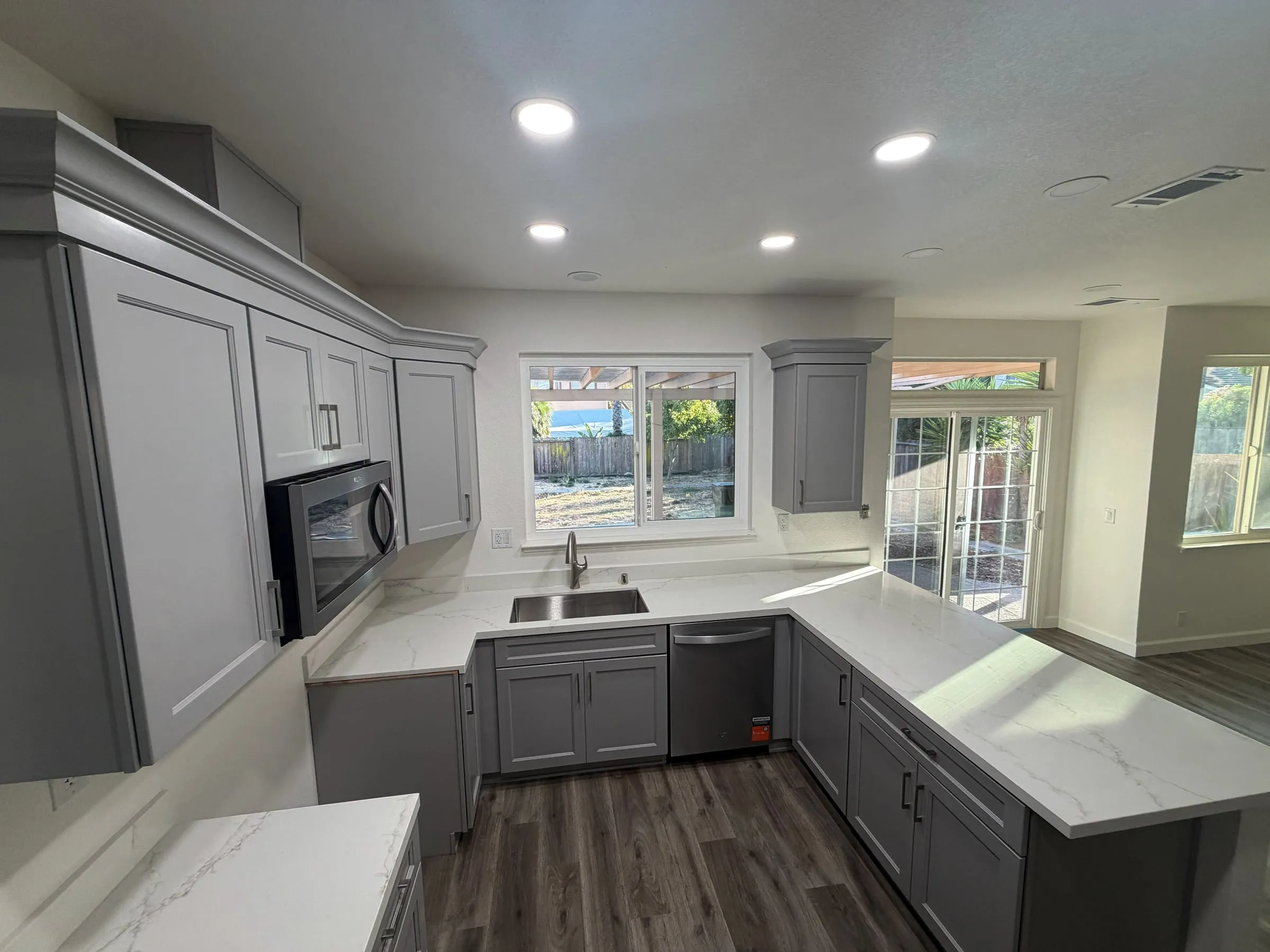 Gray shaker kitchen with quartz counters, a stainless microwave and the sink under a window