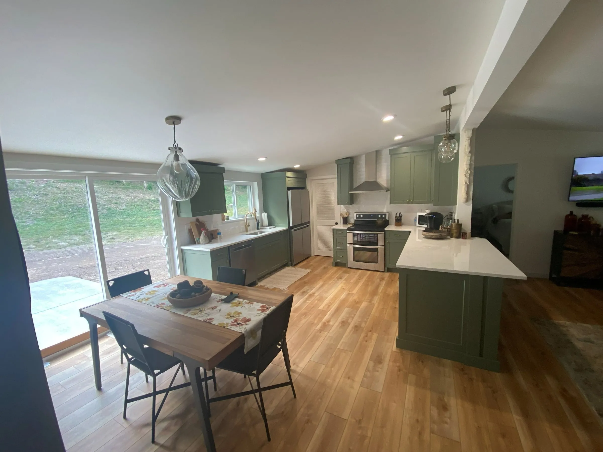 Remodeled kitchen with sage green shaker cabinets, a quartz island, pendant lights and wood-look floors
