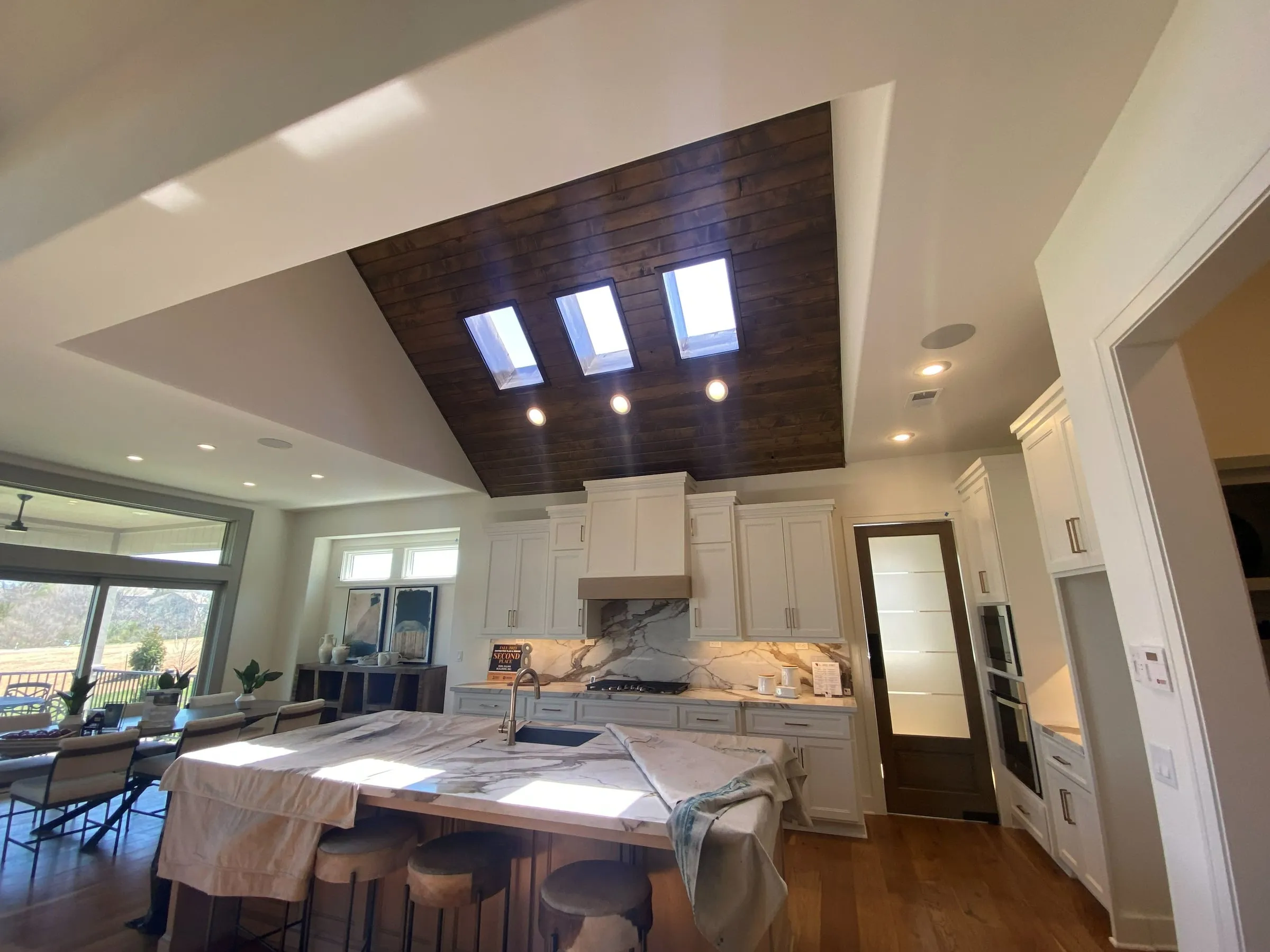 Kitchen remodel with a large island, skylights in a wood-plank ceiling and white cabinets