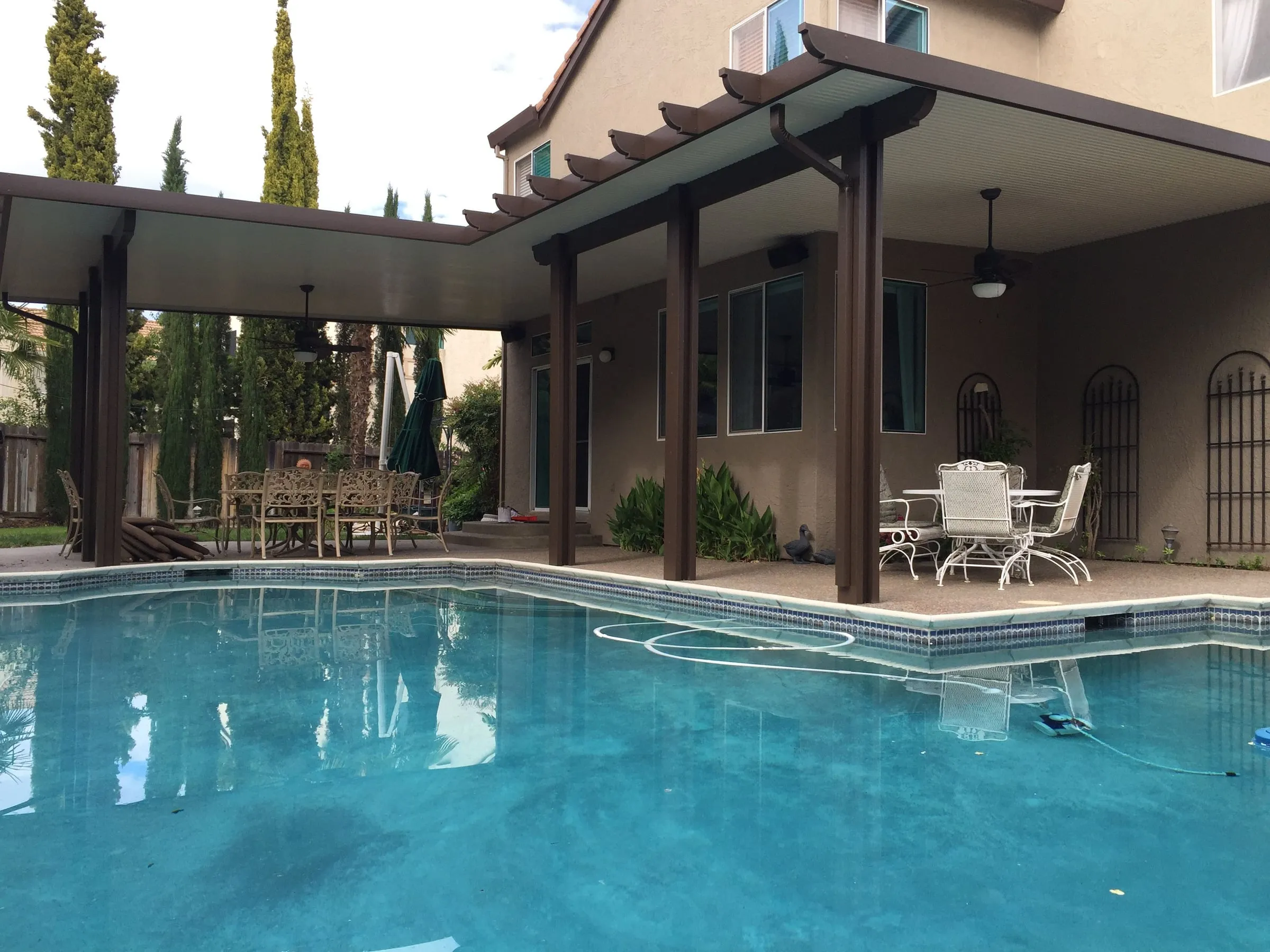 L-shaped patio cover with dark posts wrapping a poolside patio