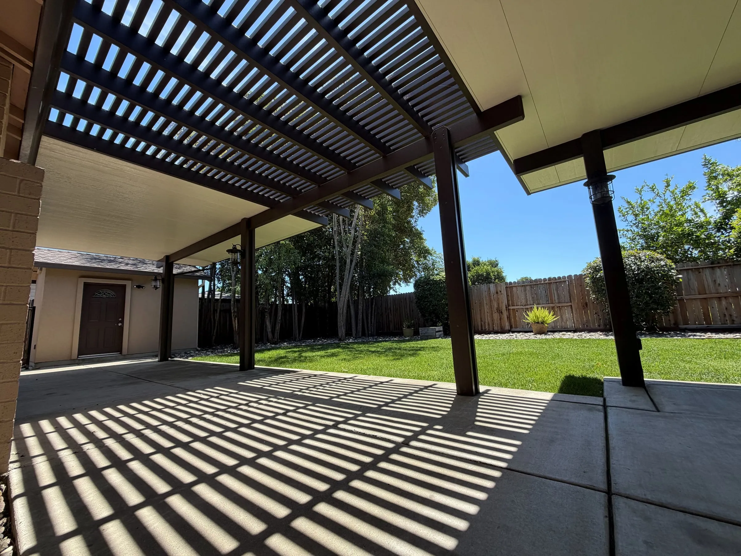 Lattice patio cover casting striped shade across a backyard patio