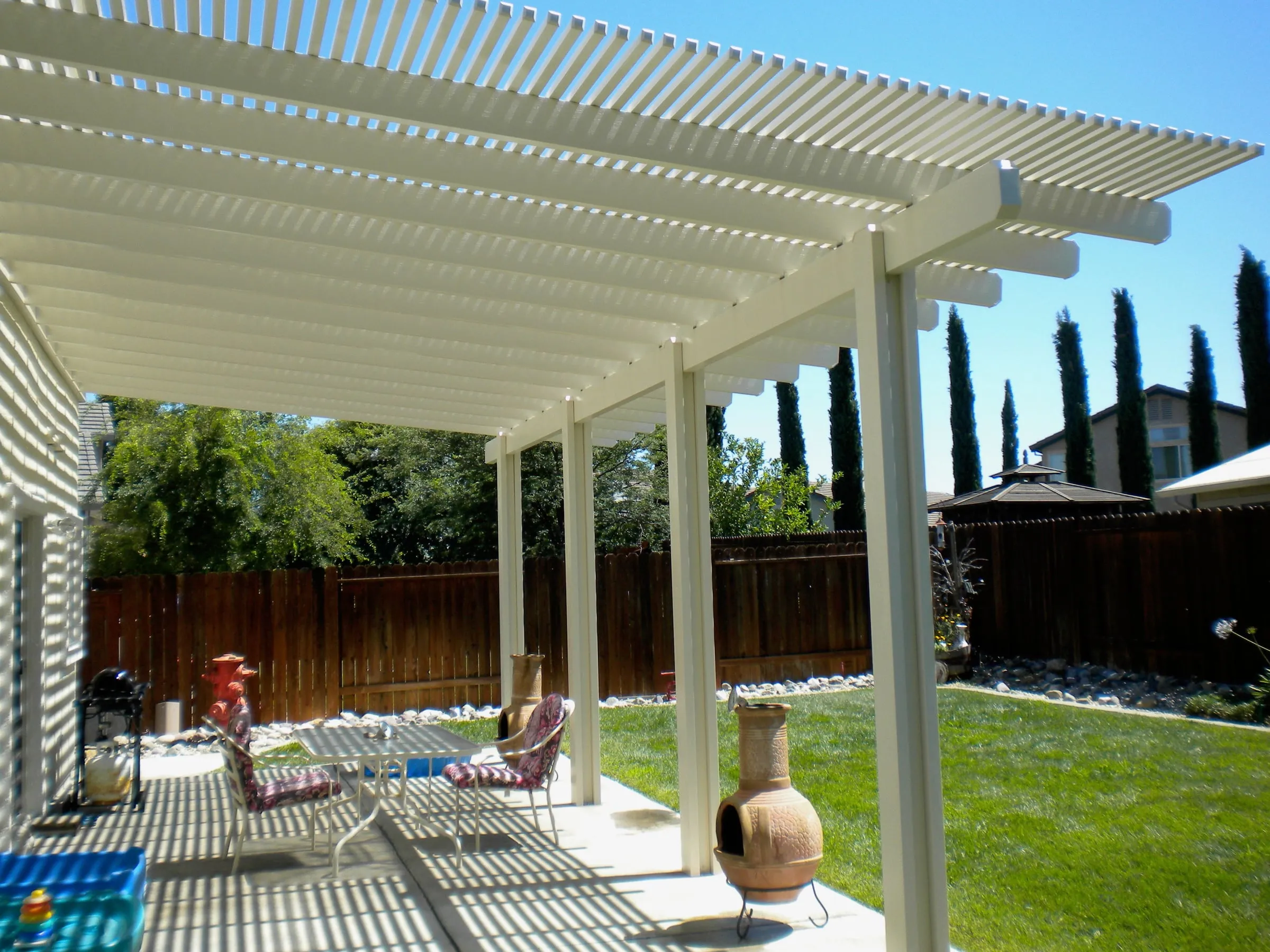 White lattice pergola over a backyard patio with lawn