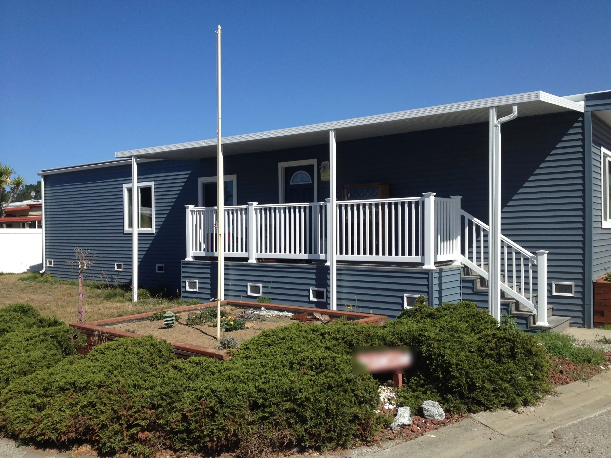 Mobile home with new blue siding, white trim and a railed front deck