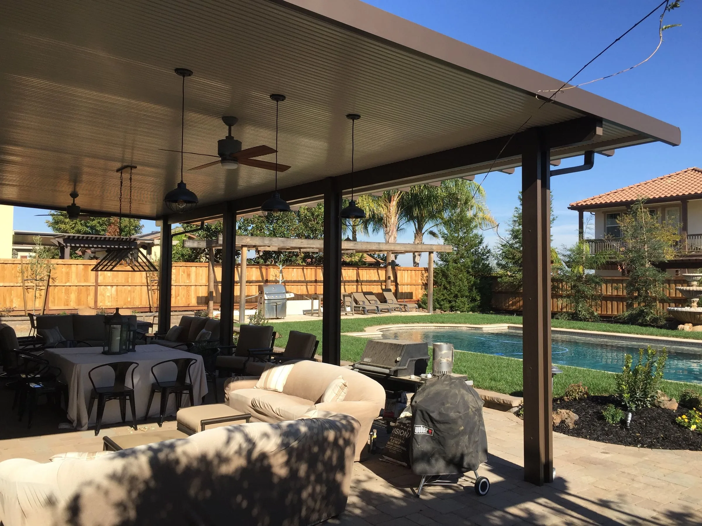 Large patio cover with ceiling fans over an outdoor living room beside a pool