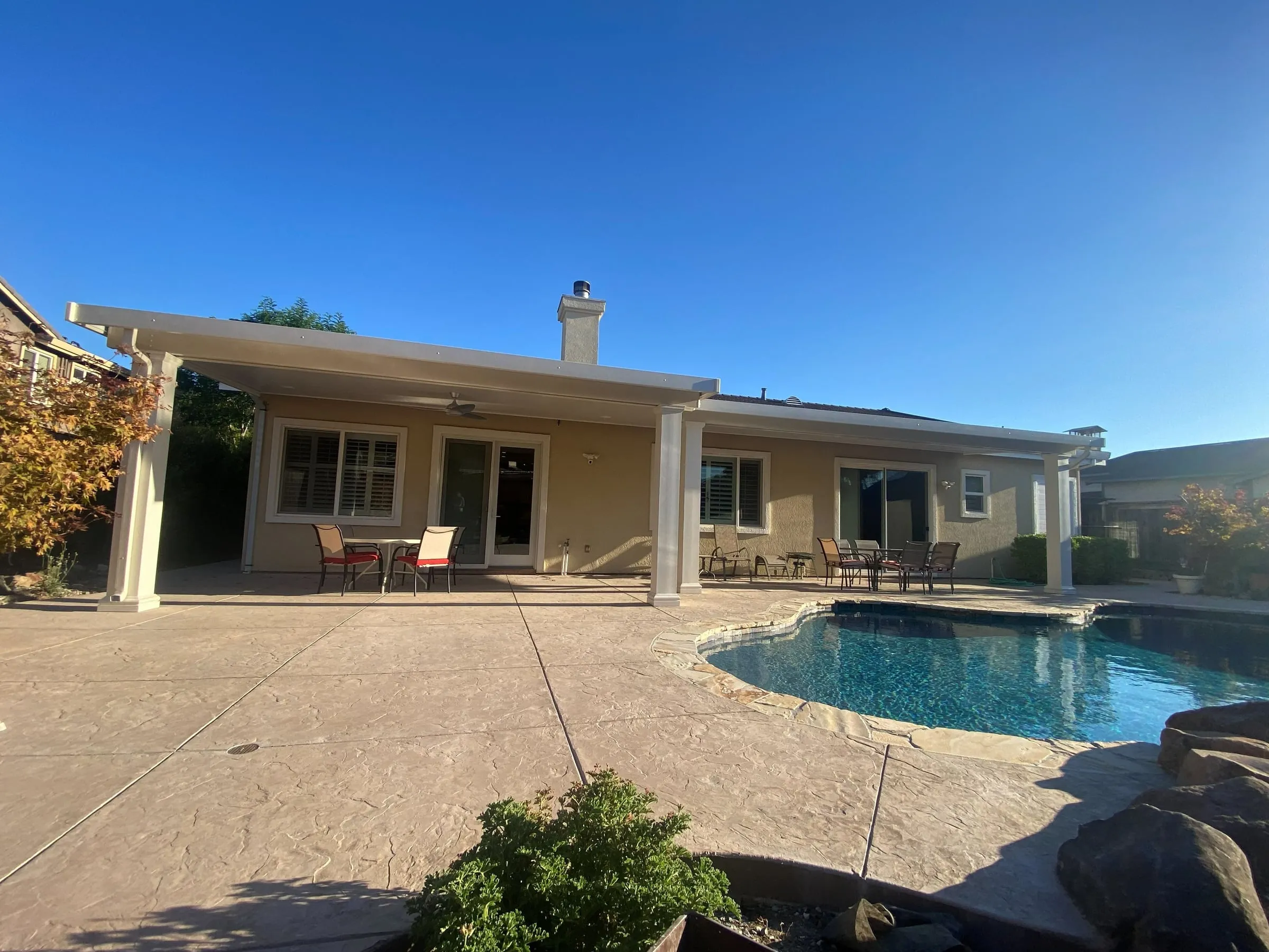 Long white patio cover across the back of a home beside a pool