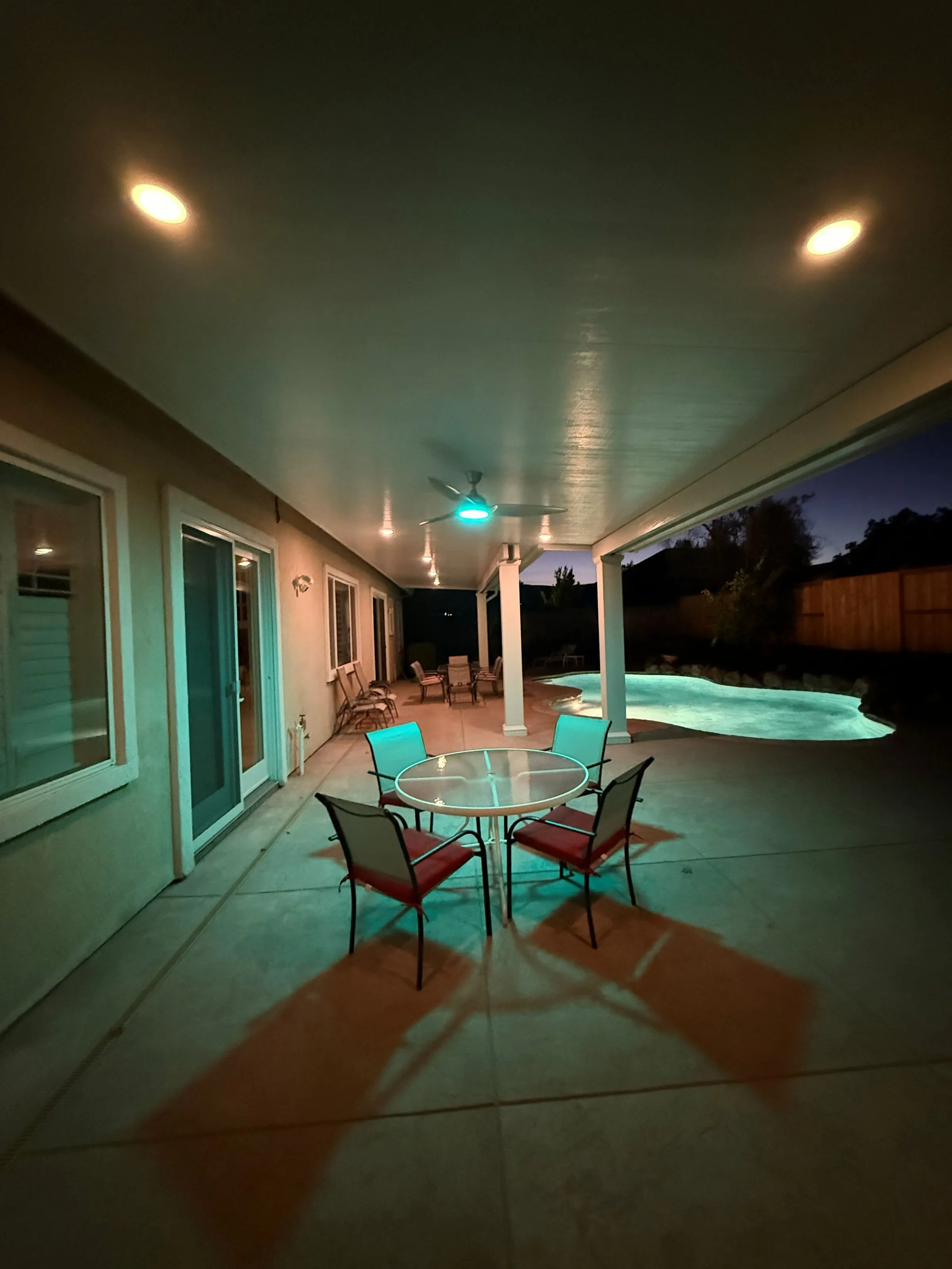 Patio cover with recessed lights glowing at night beside a lit pool