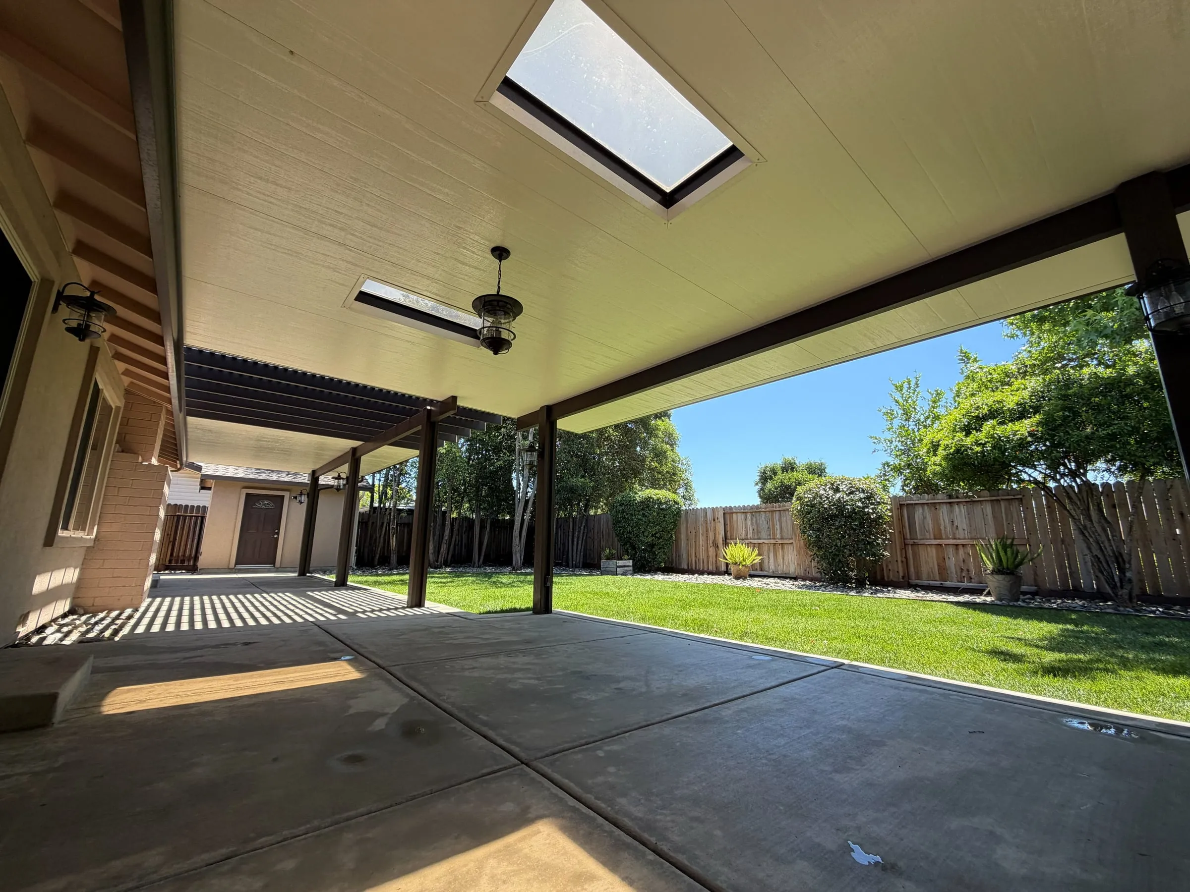 Insulated patio cover with skylight panels and a ceiling fan over a concrete patio