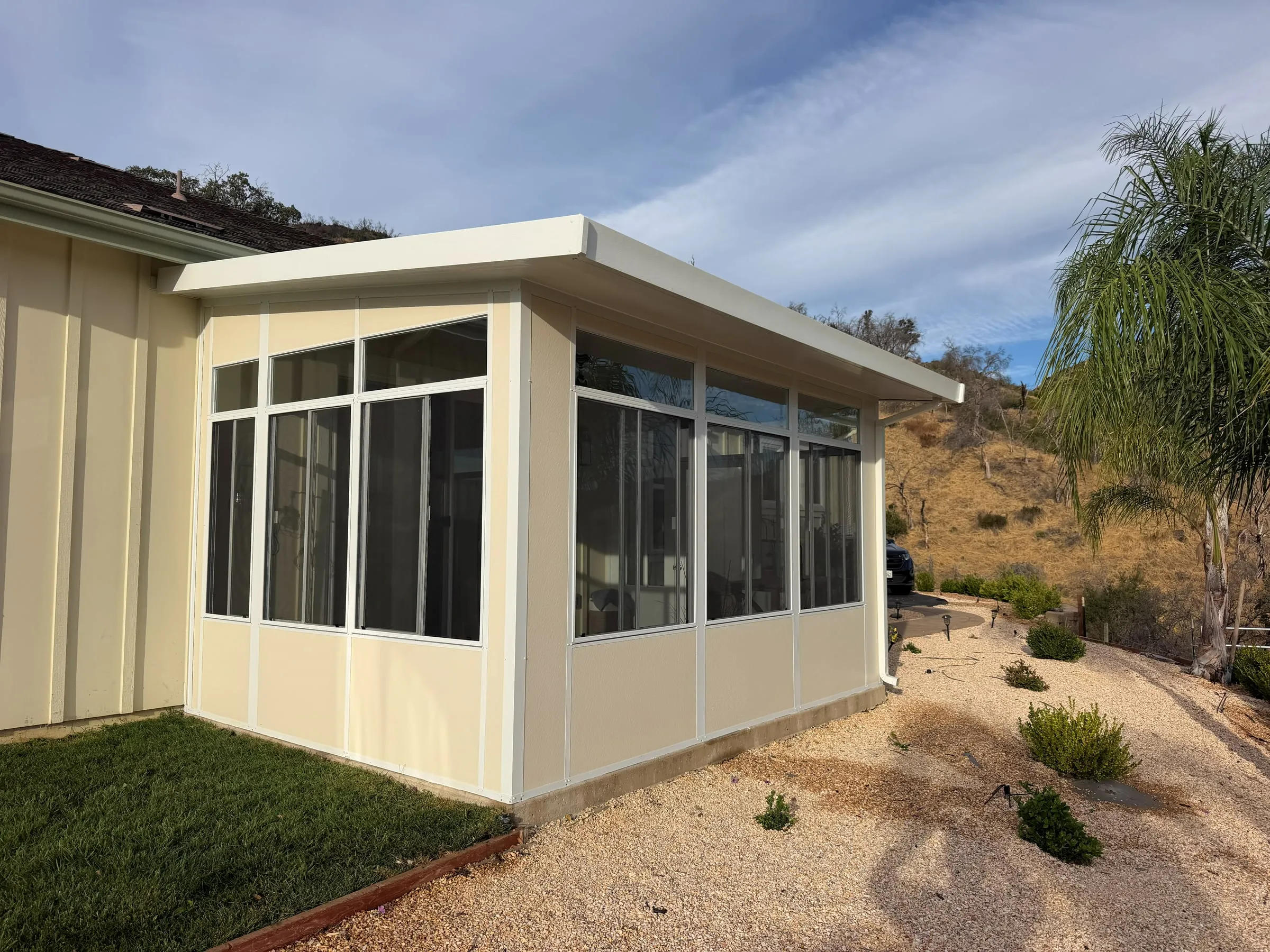 Sunroom addition with tall windows and a flat roof beside a hillside yard