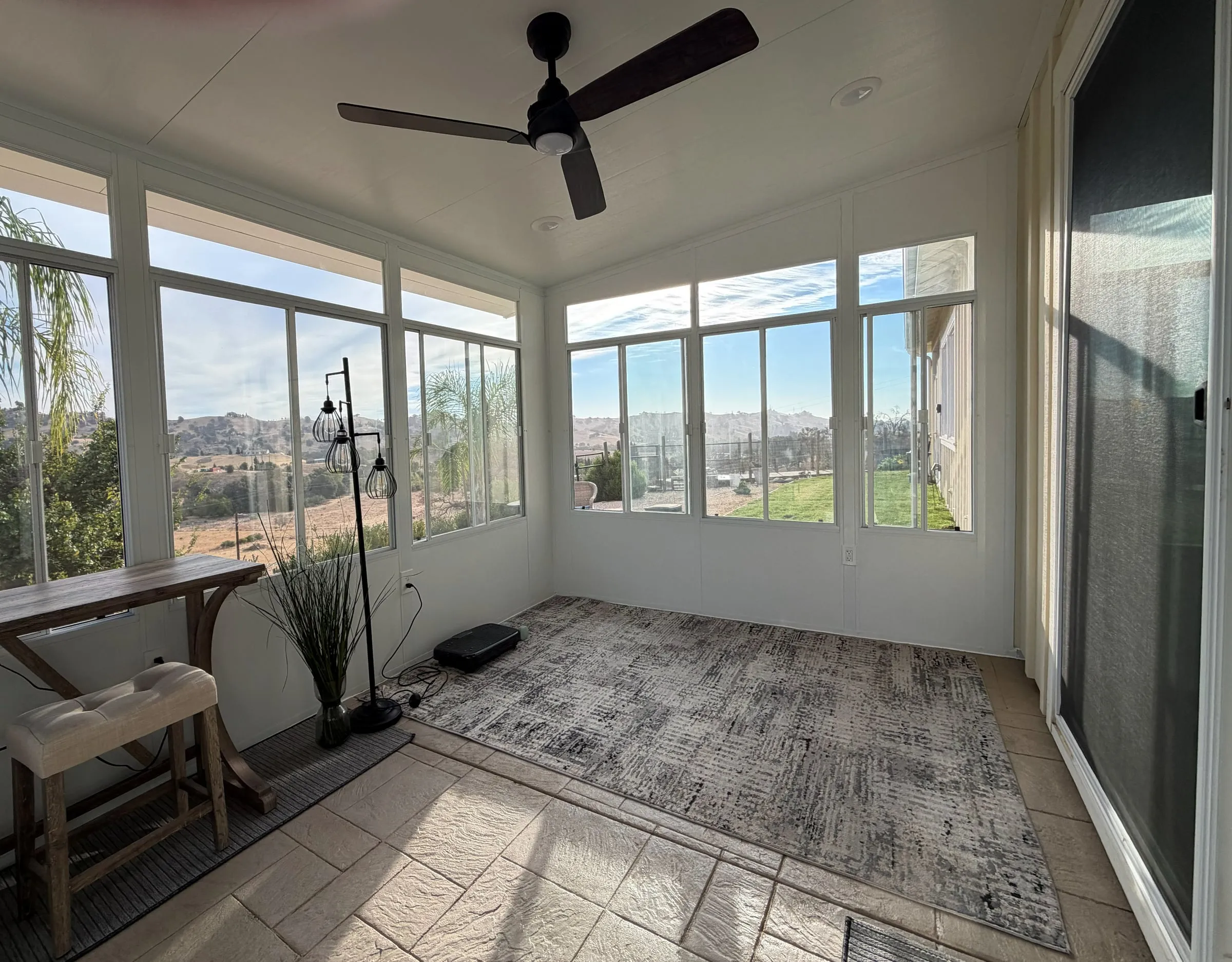 Inside a finished sunroom with a ceiling fan, windows on three sides and hillside views